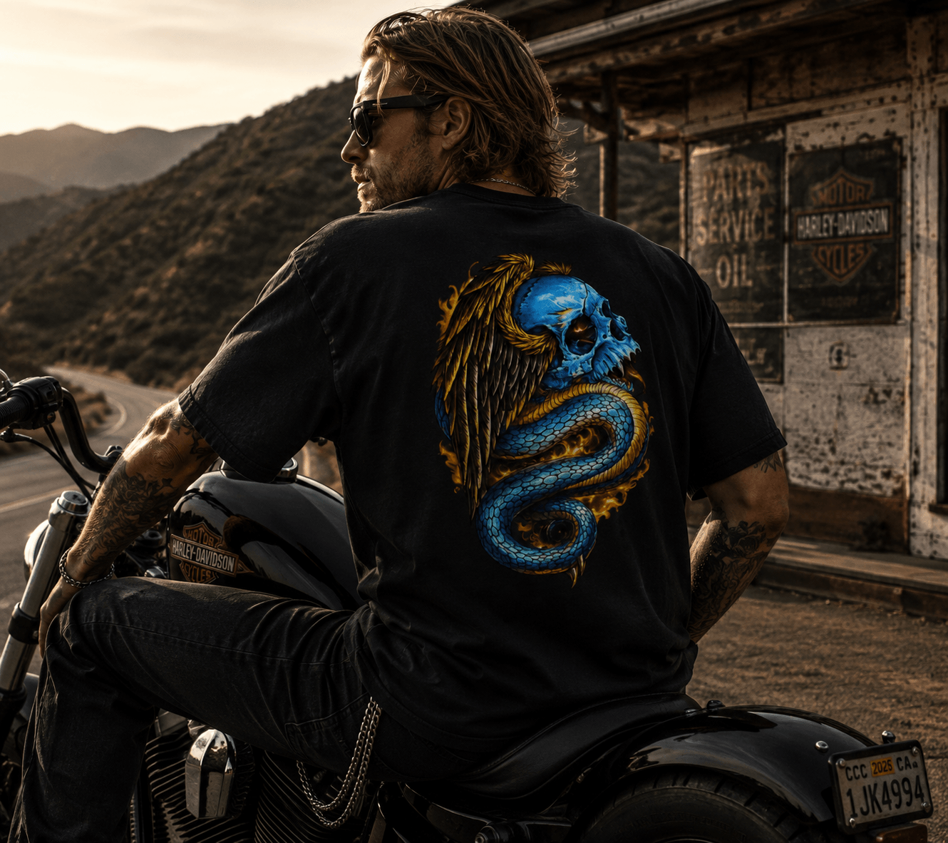 Man sitting on a motorcycle wearing a black t-shirt with a colorful design, with a scenic background.