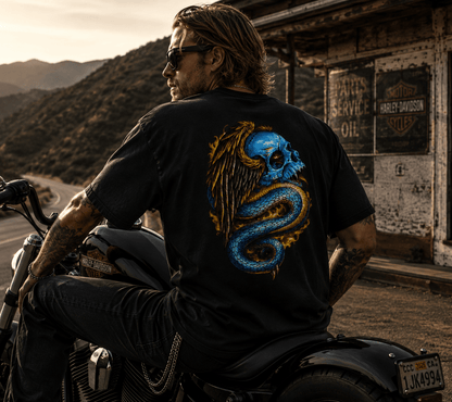 Man sitting on a motorcycle wearing a black t-shirt with a colorful design, with a scenic background.